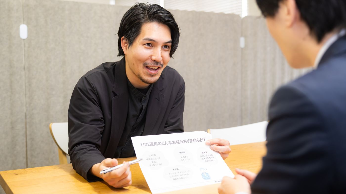 取引先の担当者に企画の提案資料を示して説明する社員